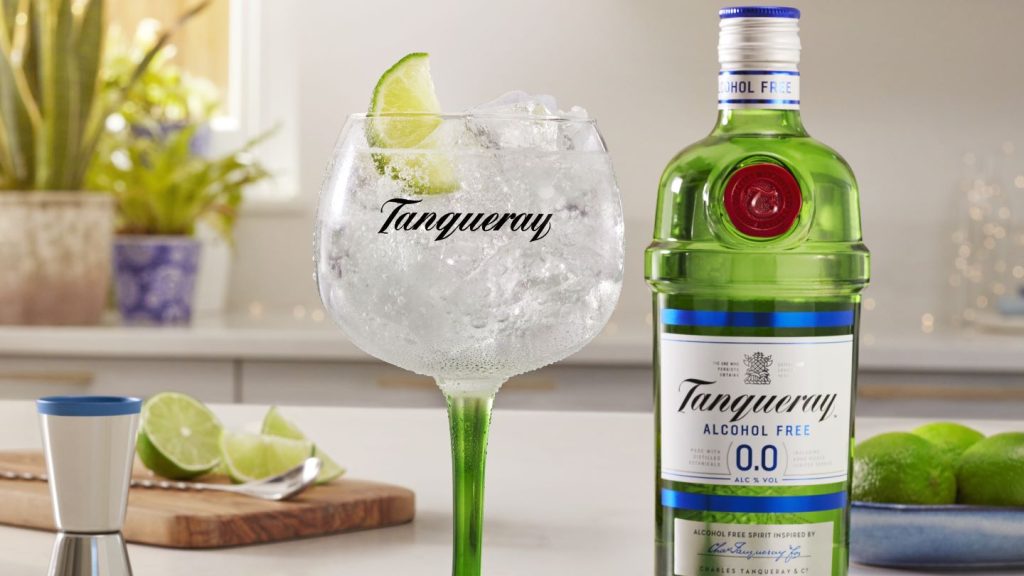 gin glass with lime slice and Tanqueray 0.0 bottle on white table. 