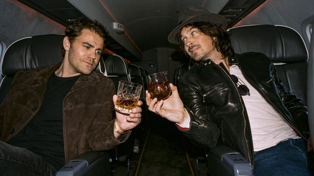 two men in airplane toasting with glasses of bourbon. 