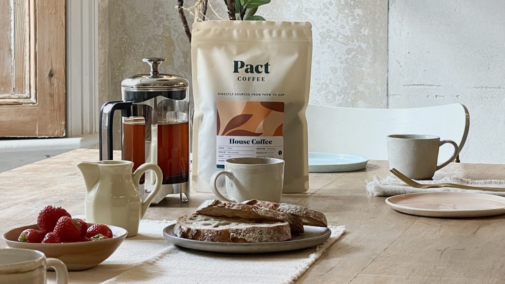 Pact Coffee brand packet with coffee pot, plate of bread and coffee cup on table.